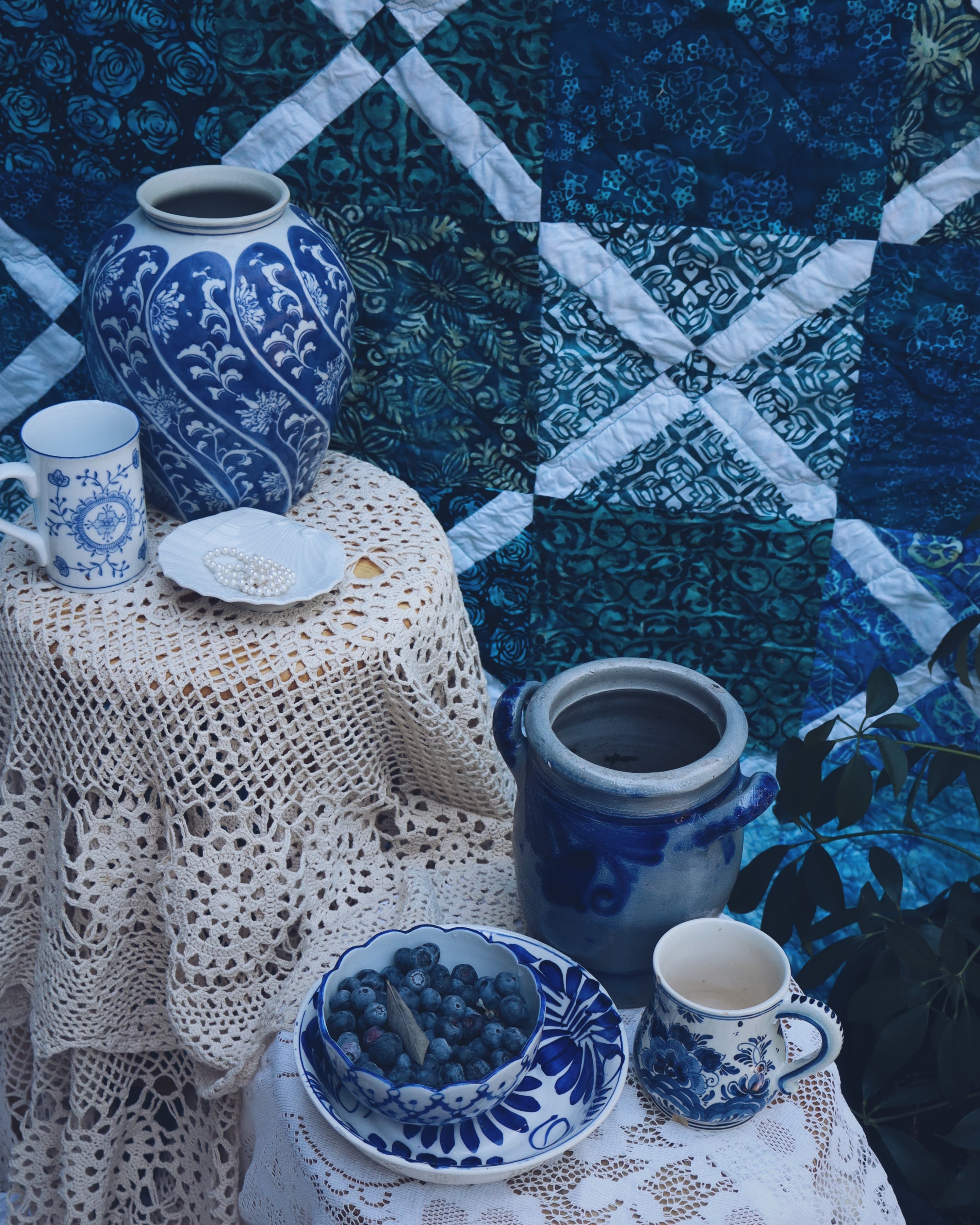 Blue and white ceramic items on a table with a patterned blue fabric background